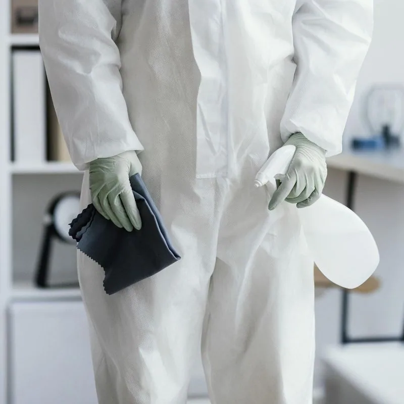 Person in white hazmat suit holding spray bottle and cleaning cloth.