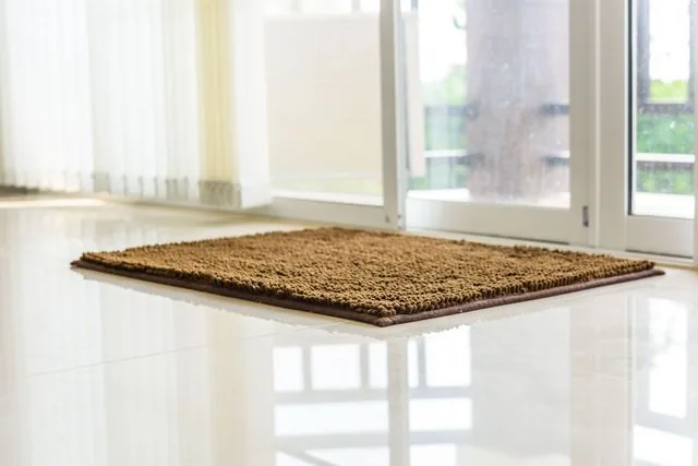 Brown rectangular rug on a shiny white tile floor in front of a glass sliding door.