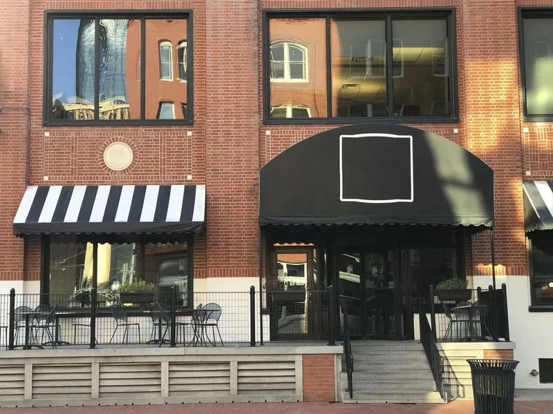 Brick building with black awnings over entrances and windows reflecting other buildings.