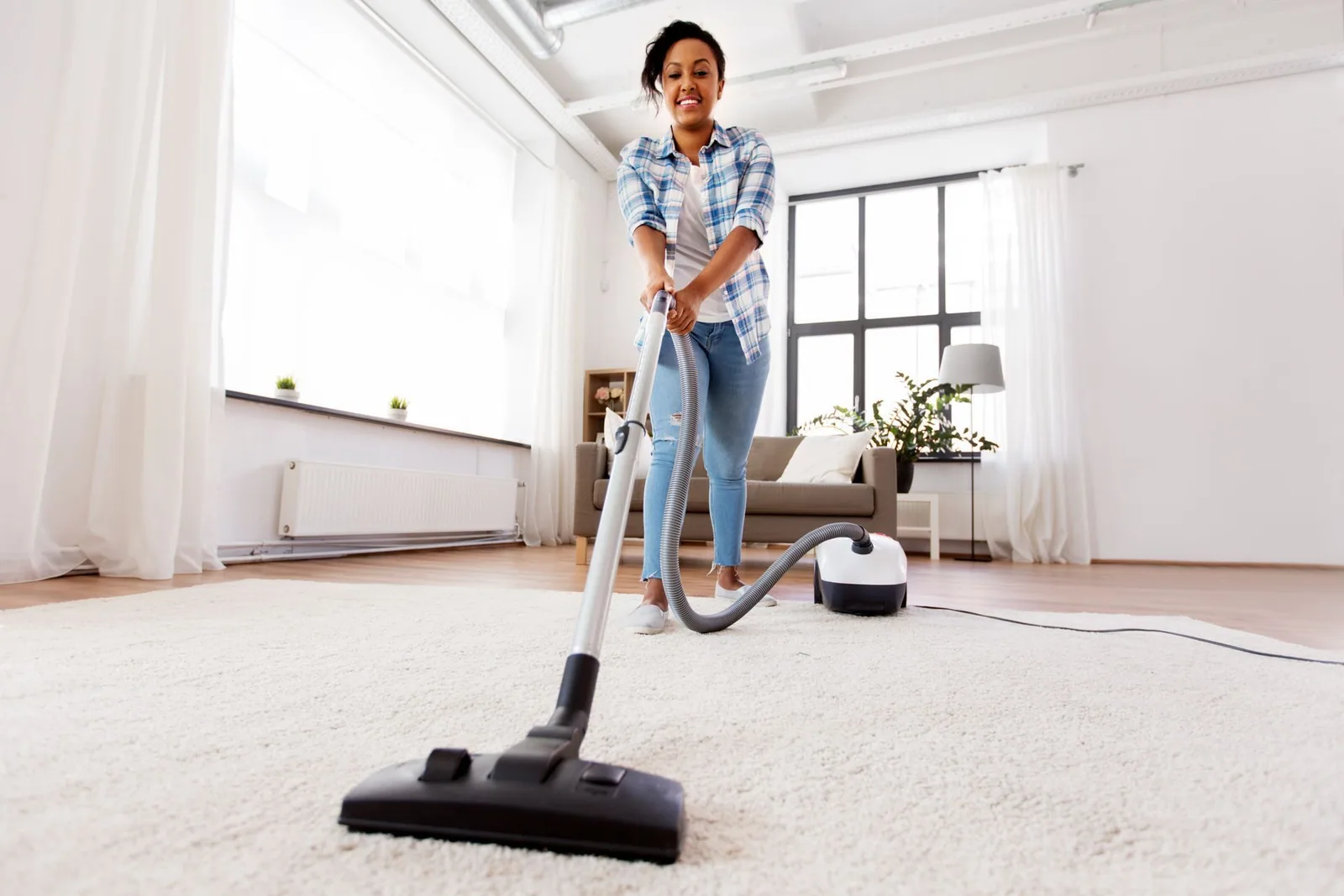 Person vacuuming a white carpet in a bright, modern living room.