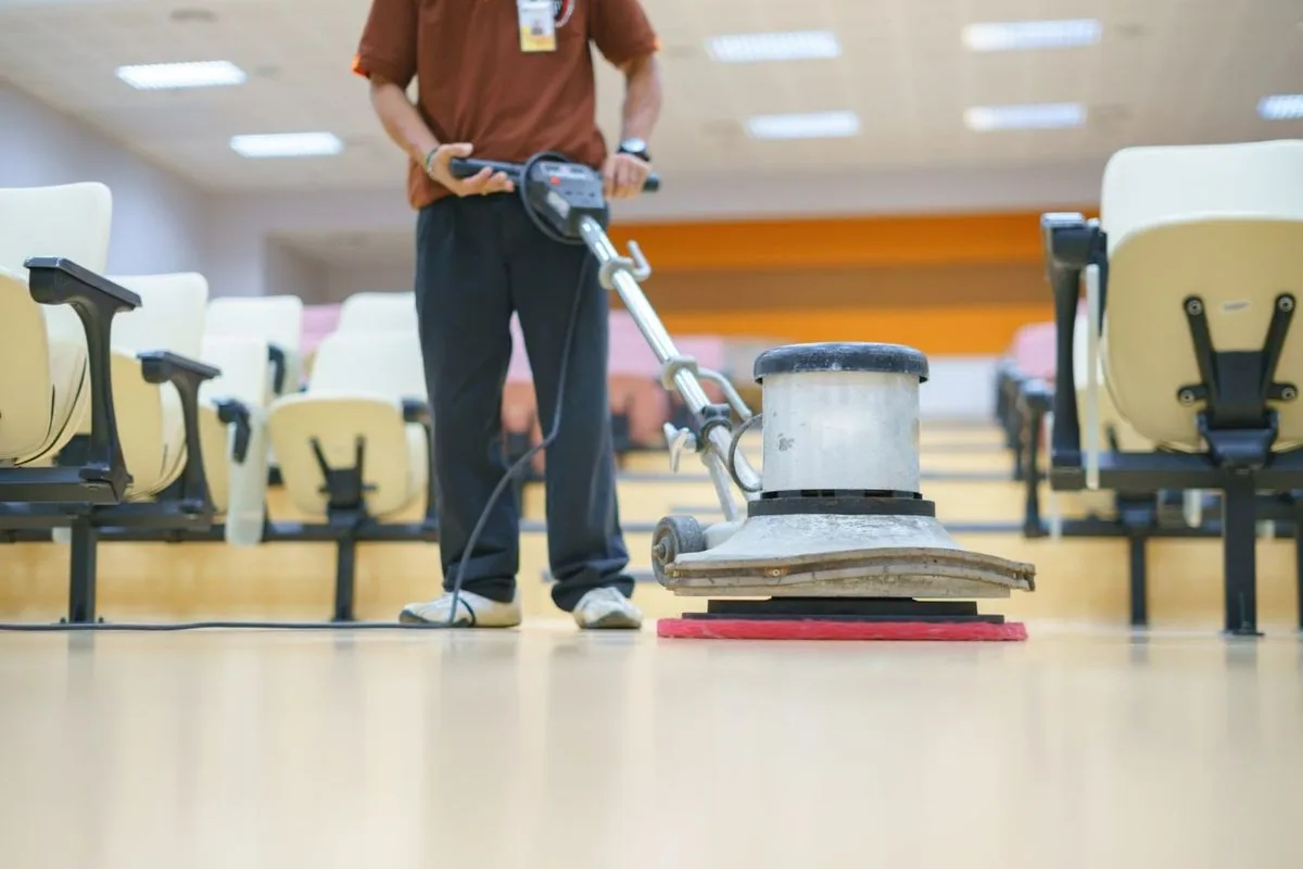 Person cleaning a brightly lit room with a floor polisher.