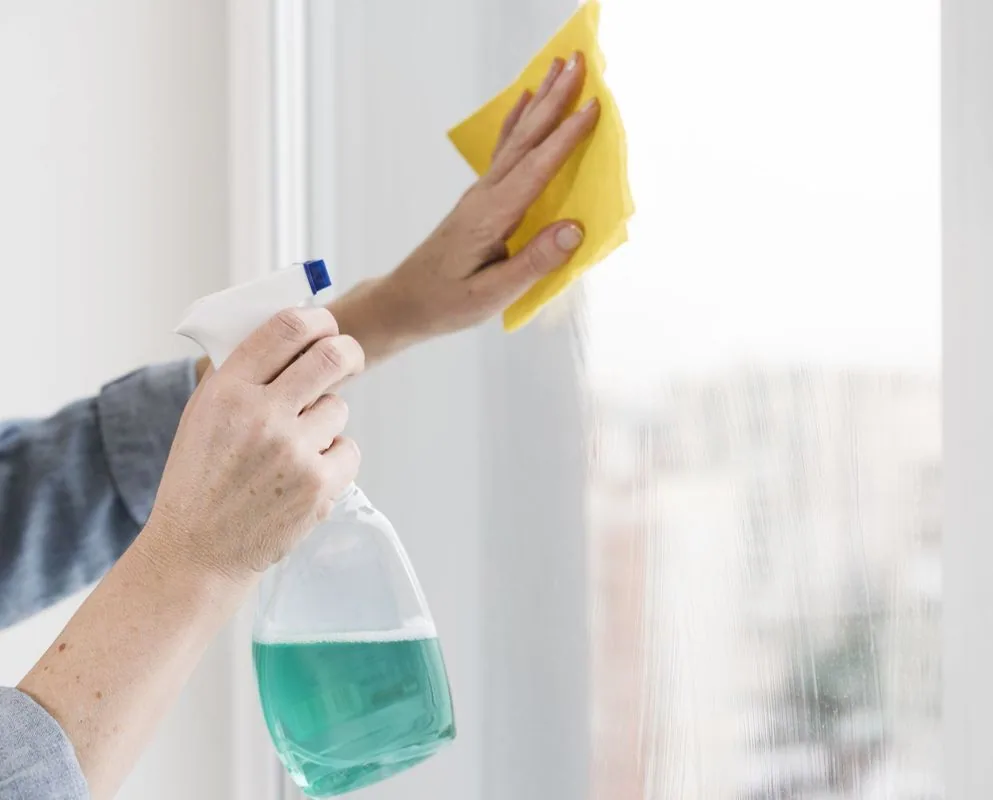 Person cleaning a window with a spray bottle and yellow cloth.