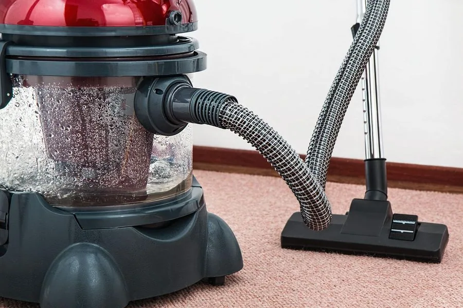 Red and black vacuum cleaner with hose and nozzle on pink carpet.
