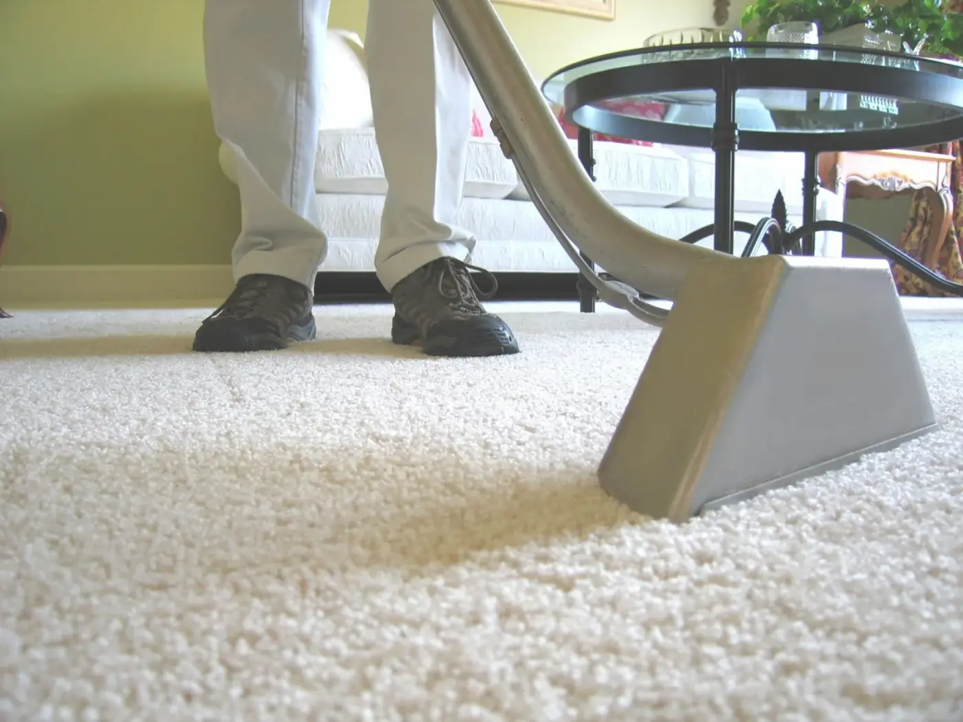 Person vacuuming white carpet with gray vacuum head; indoor setting.