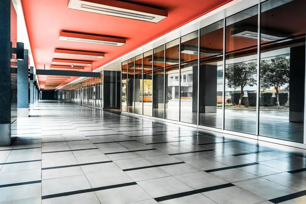 Empty hallway with red ceiling, large windows reflecting trees, and tiled floor.