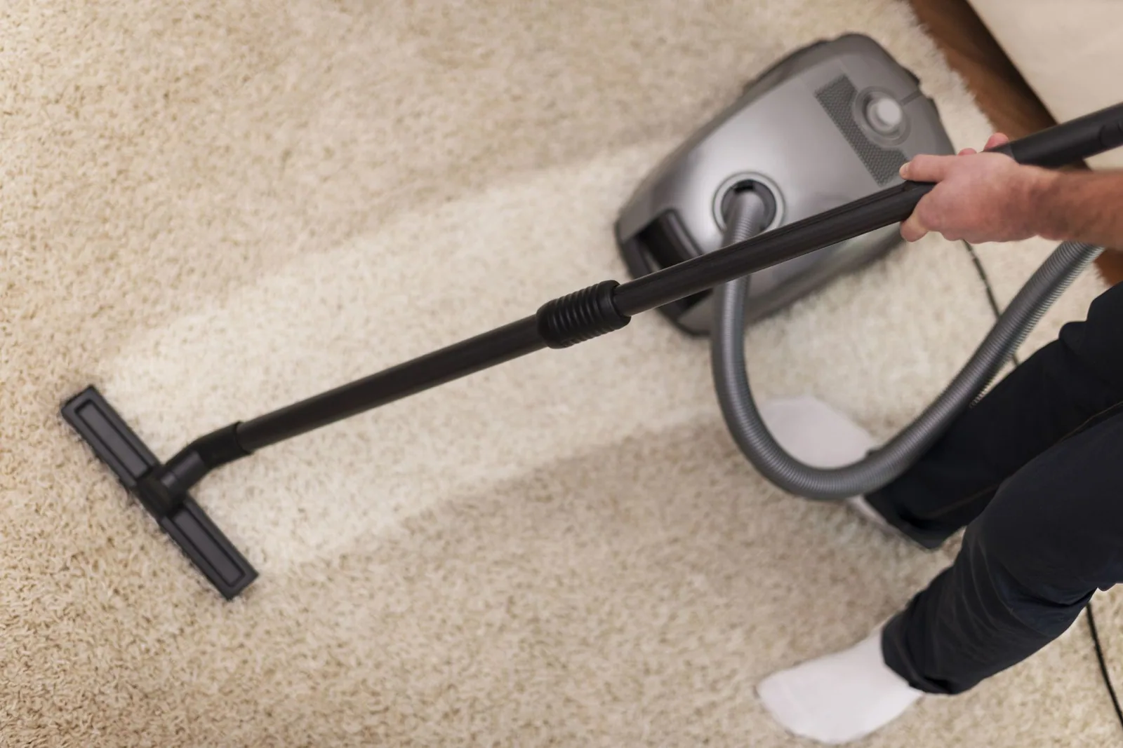 Vacuuming a beige carpet with a black vacuum cleaner, leaving a clean path.
