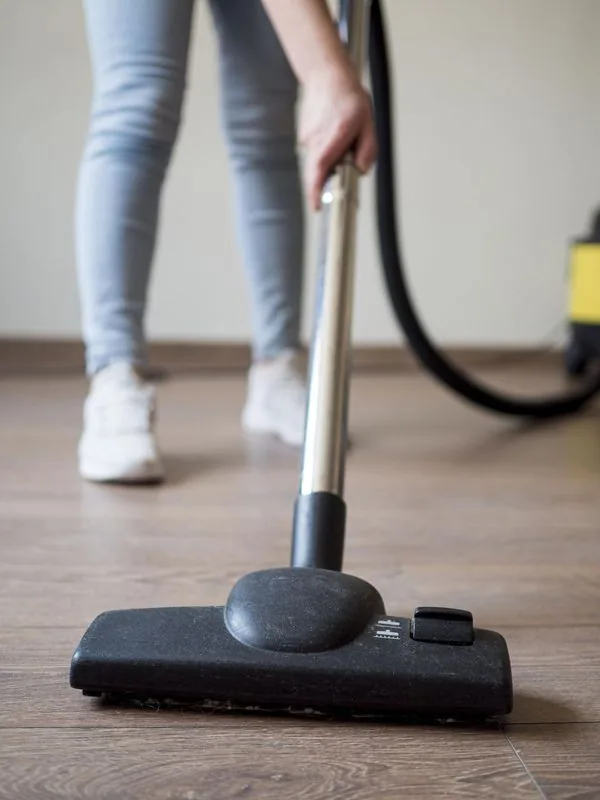 Person vacuums a wooden floor with a black vacuum cleaner.